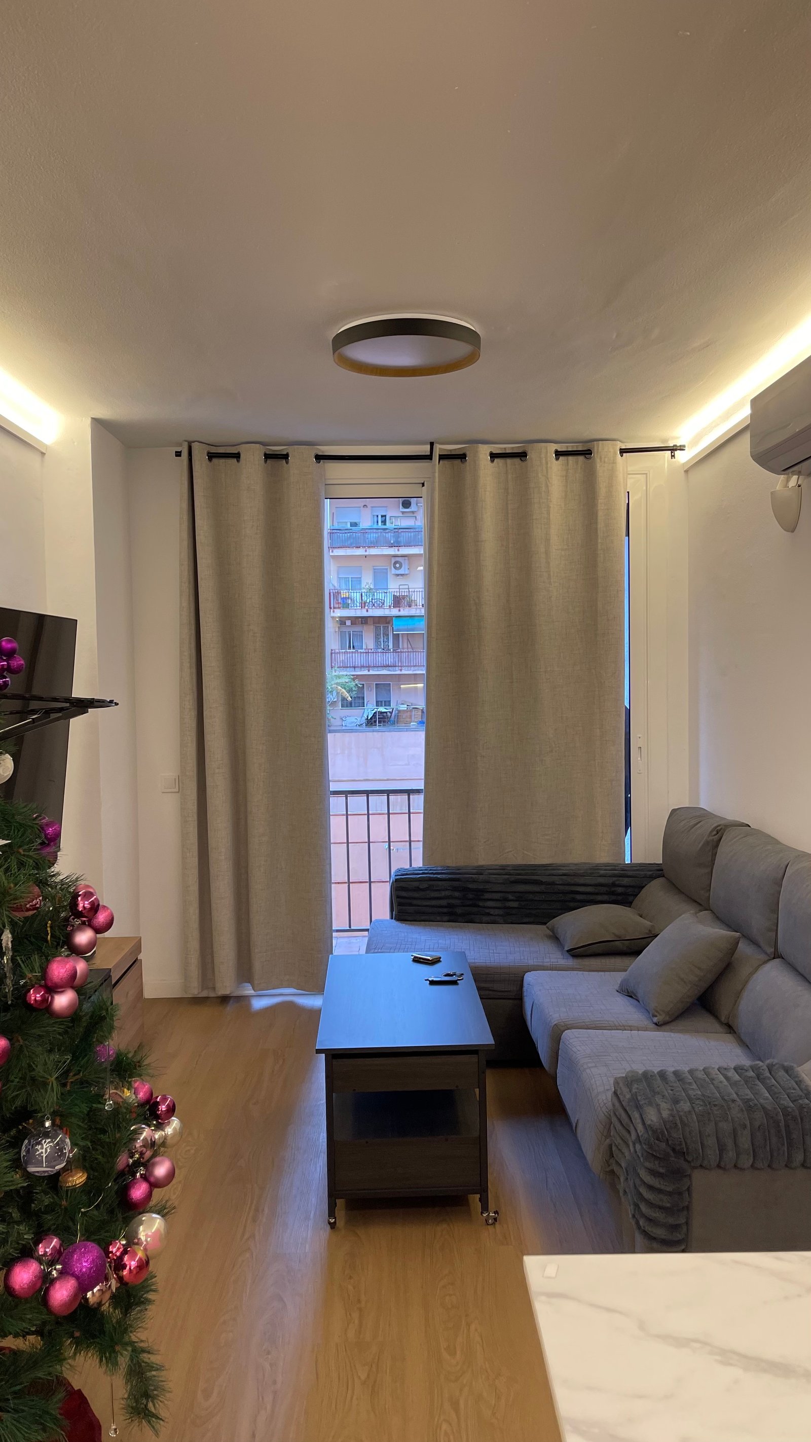Zona de estar con sofá gris y ventanal a la calle